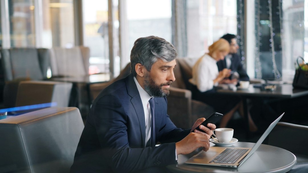 Man in a suit works on his phone at a cafe table.
