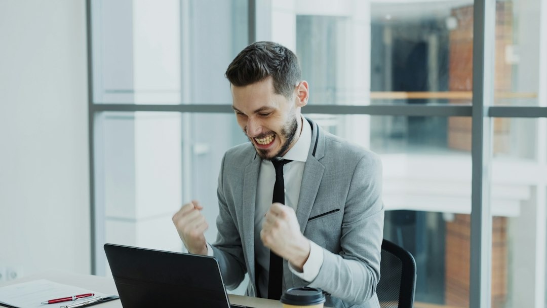 Young businessman clenches fists in excitement at laptop.
