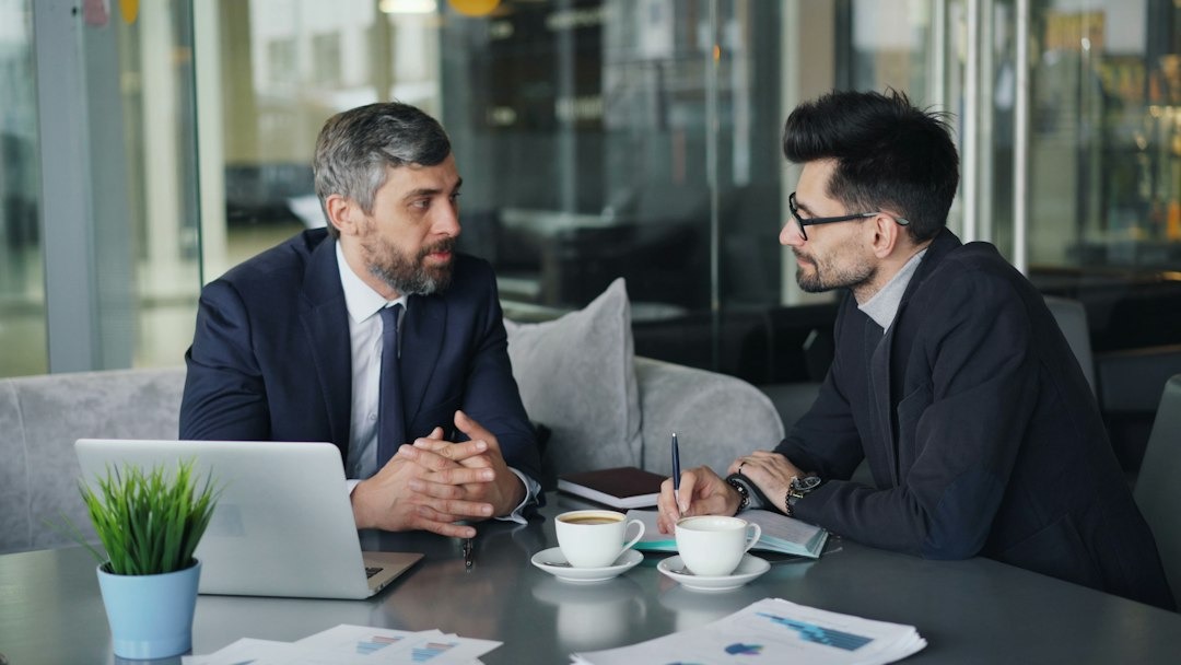 Two men discuss business over coffee and documents.