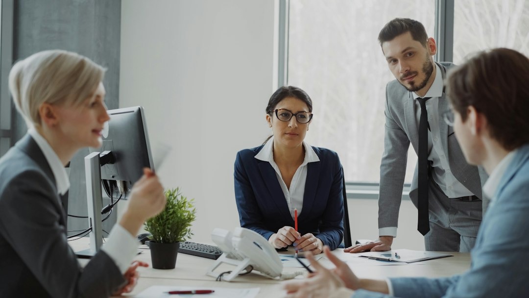 Three professionals in a modern office discussing business at a conference table.